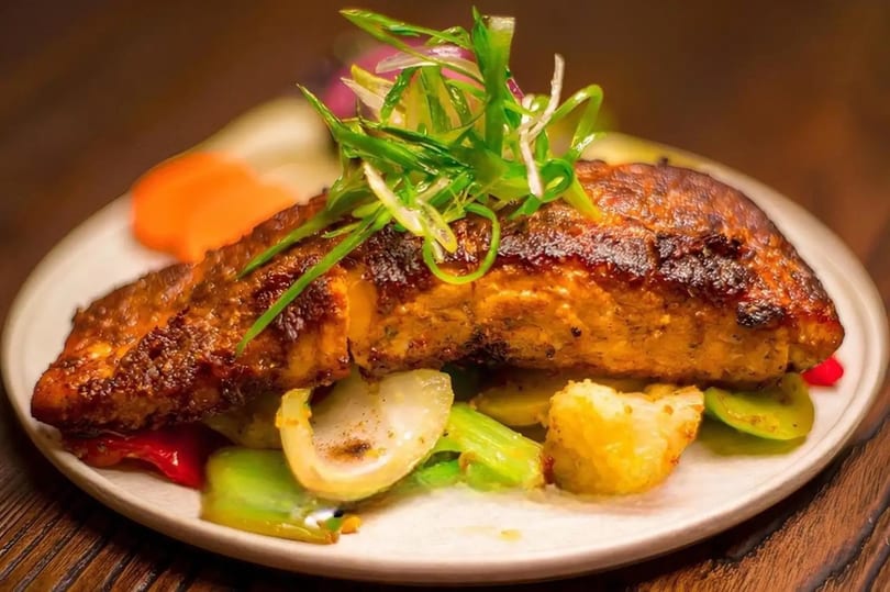 Grilled fish fillet topped with green onions, served with roasted vegetables on a white plate.