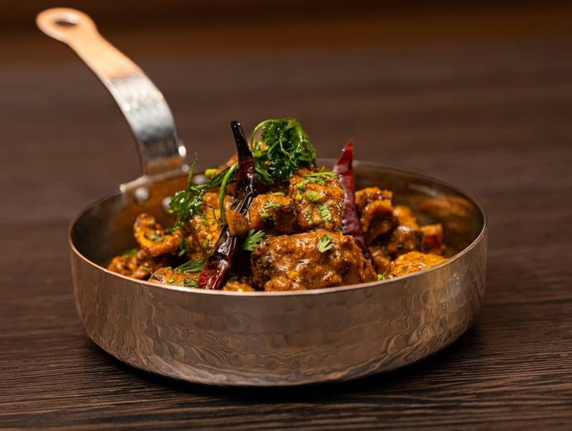 Spicy Indian curry with dried red chilies and fresh cilantro in a hammered metal serving dish.