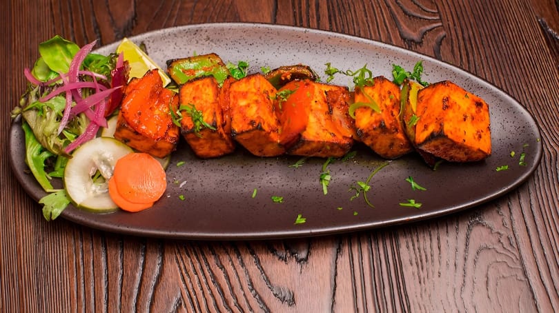 Grilled paneer tikka with bell peppers, onions, and a side salad on a dark plate.